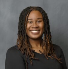 A UNC Charlotte student smiles confidently in a studio portrait against a gray backdrop.