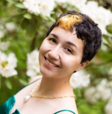 A UNC Charlotte student smiles in front of blooming white flowers on campus.