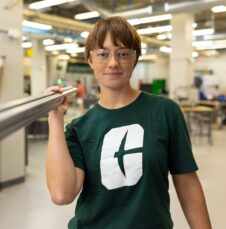 A UNC Charlotte student in safety glasses holds metal tubing in a campus engineering lab.