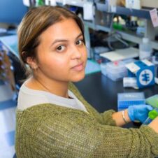 Erica-Flores UNC Charlotte student wearing gloves conducts research in a science lab using a pipette and test tubes.