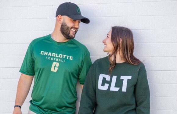 One Campus Co Two people in green tops and casual outfits leaning against a wall, smiling at each other.