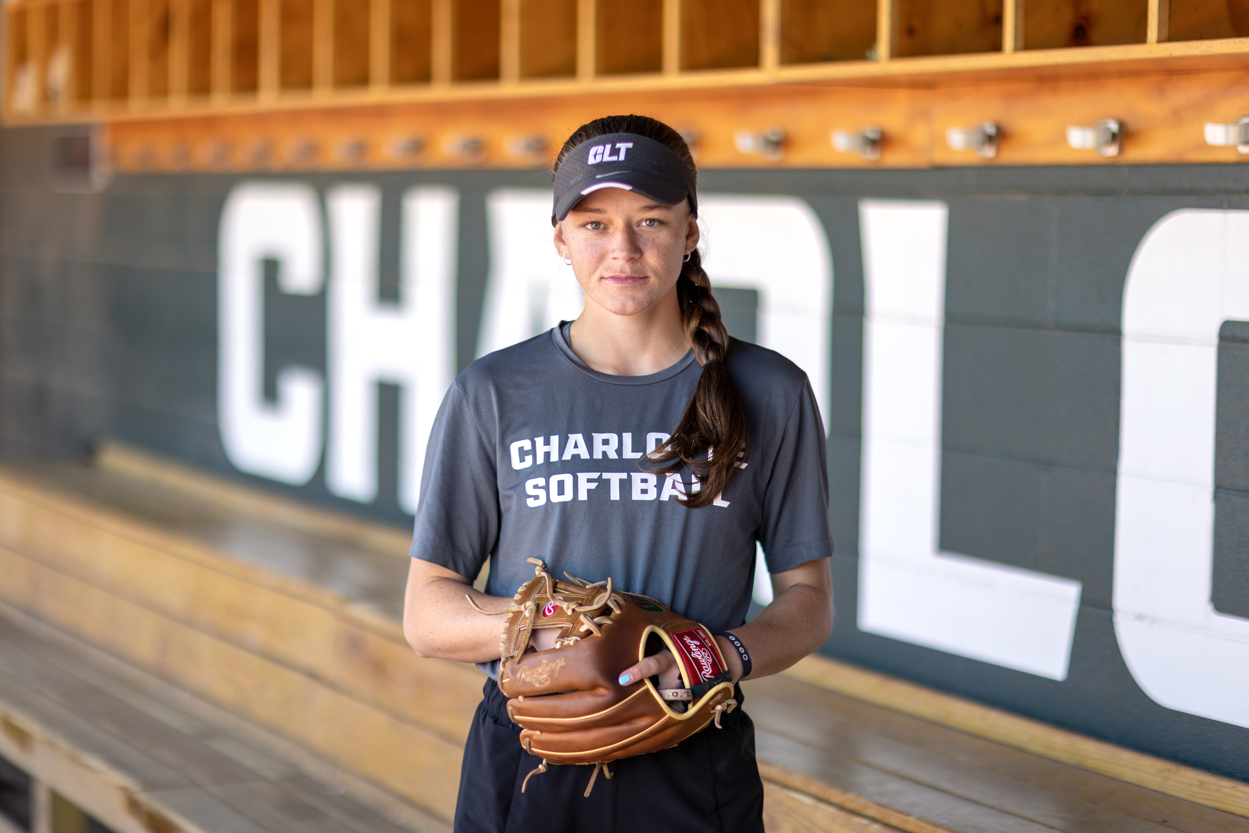 Softball player wearing their glove and looking into the camera with Charlotte written on the wall in the background.