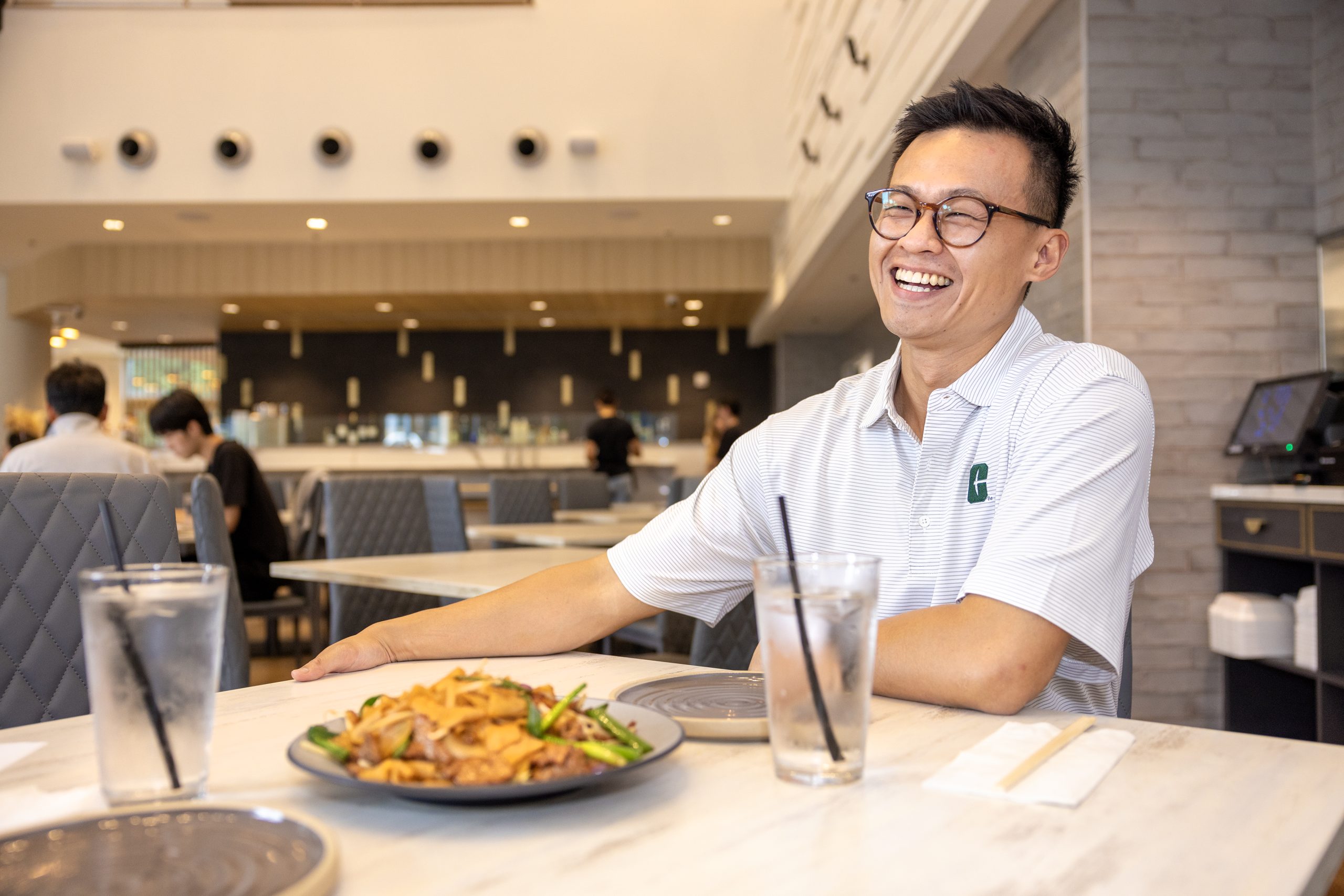 ALUM_Open Rice_240923_199_rh Man in white polo shirt sitting at a table smiling at the camera.