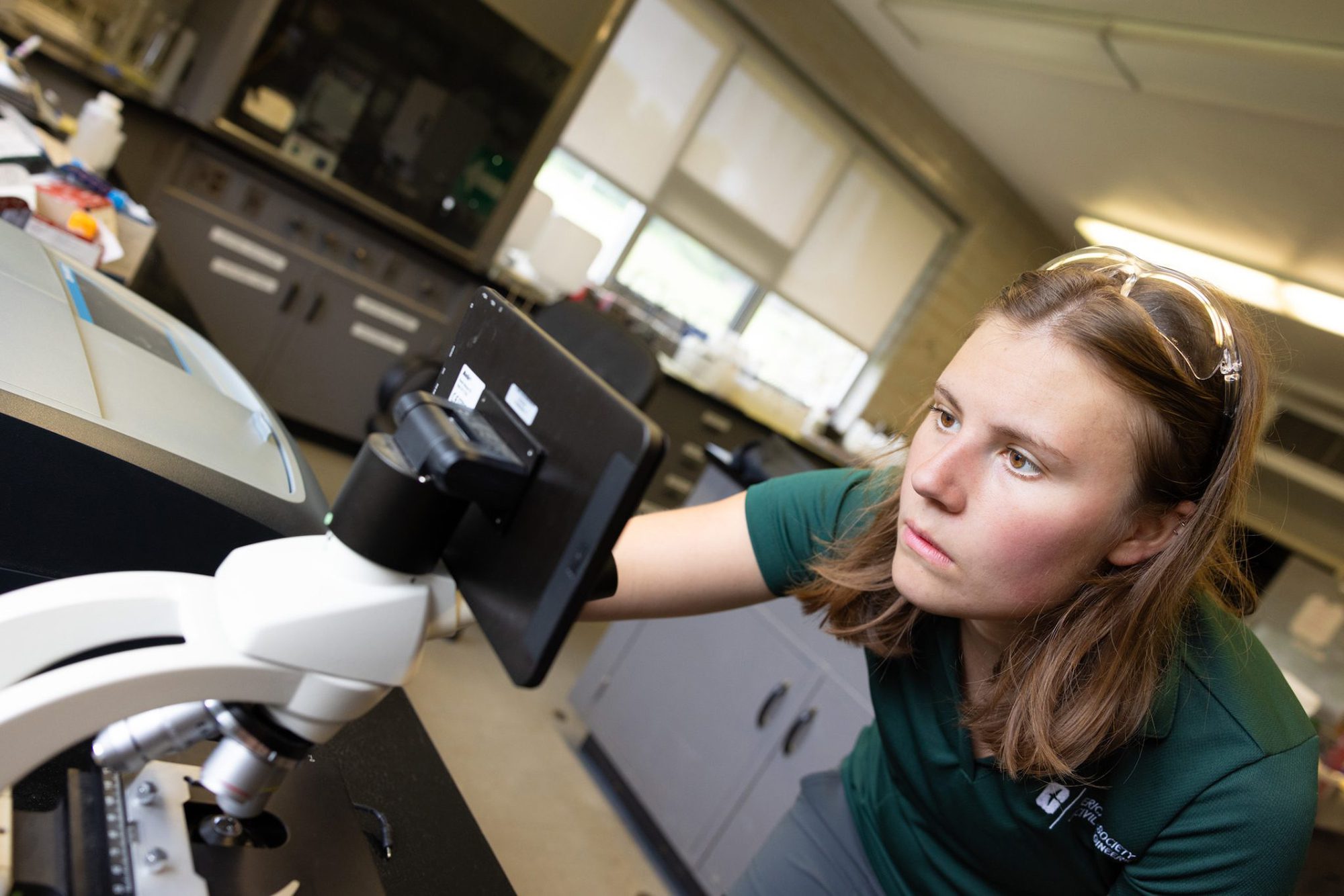 Woman in a laboratory looking through a microscope with a digital screen.