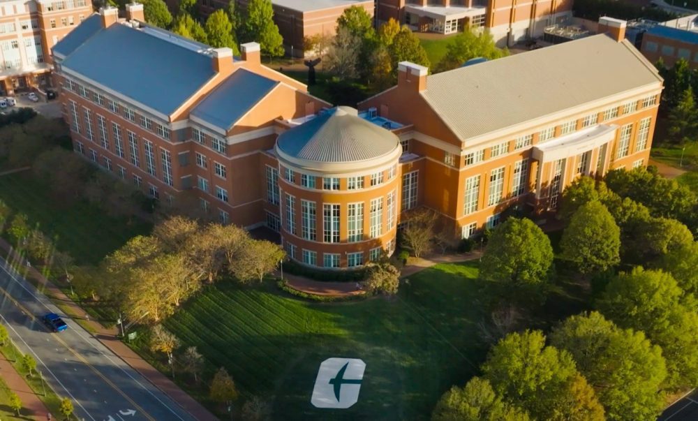 An aerial view of the UNC Charlotte campus building with a large Charlotte "C" logo on the lawn.