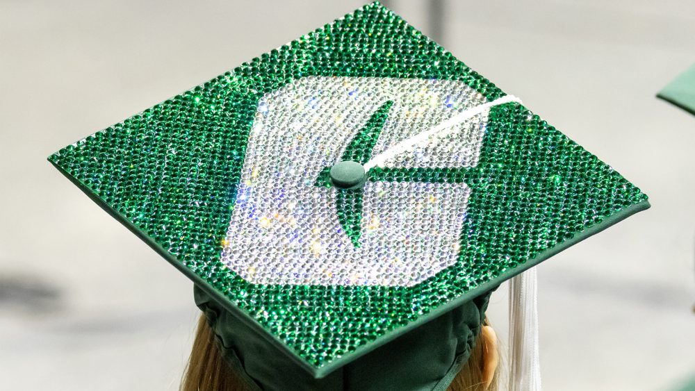 Graduation cap covered in green gems with a sparkling white “C” logo.