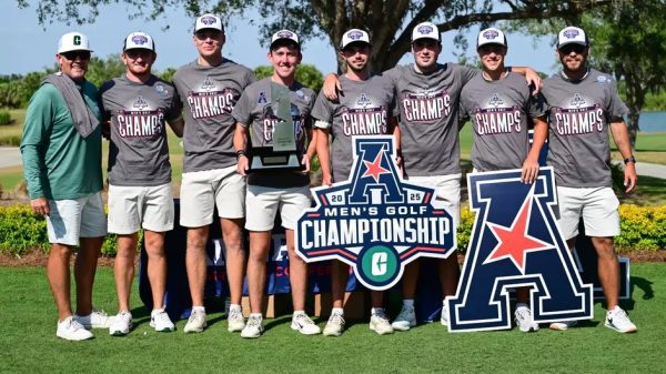 Men’s golf team in “CHAMPS” shirts poses with a trophy and championship signs.
