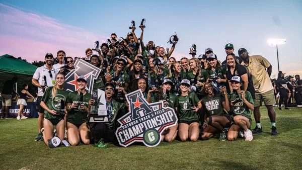 Women’s track team celebrates with trophies and a championship sign on the field.