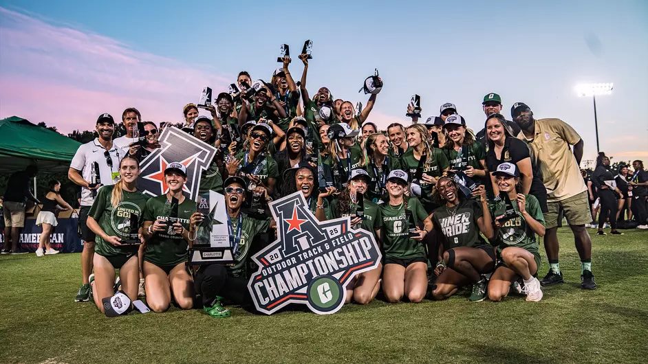 Women’s track team celebrates with trophies and a championship sign on the field.