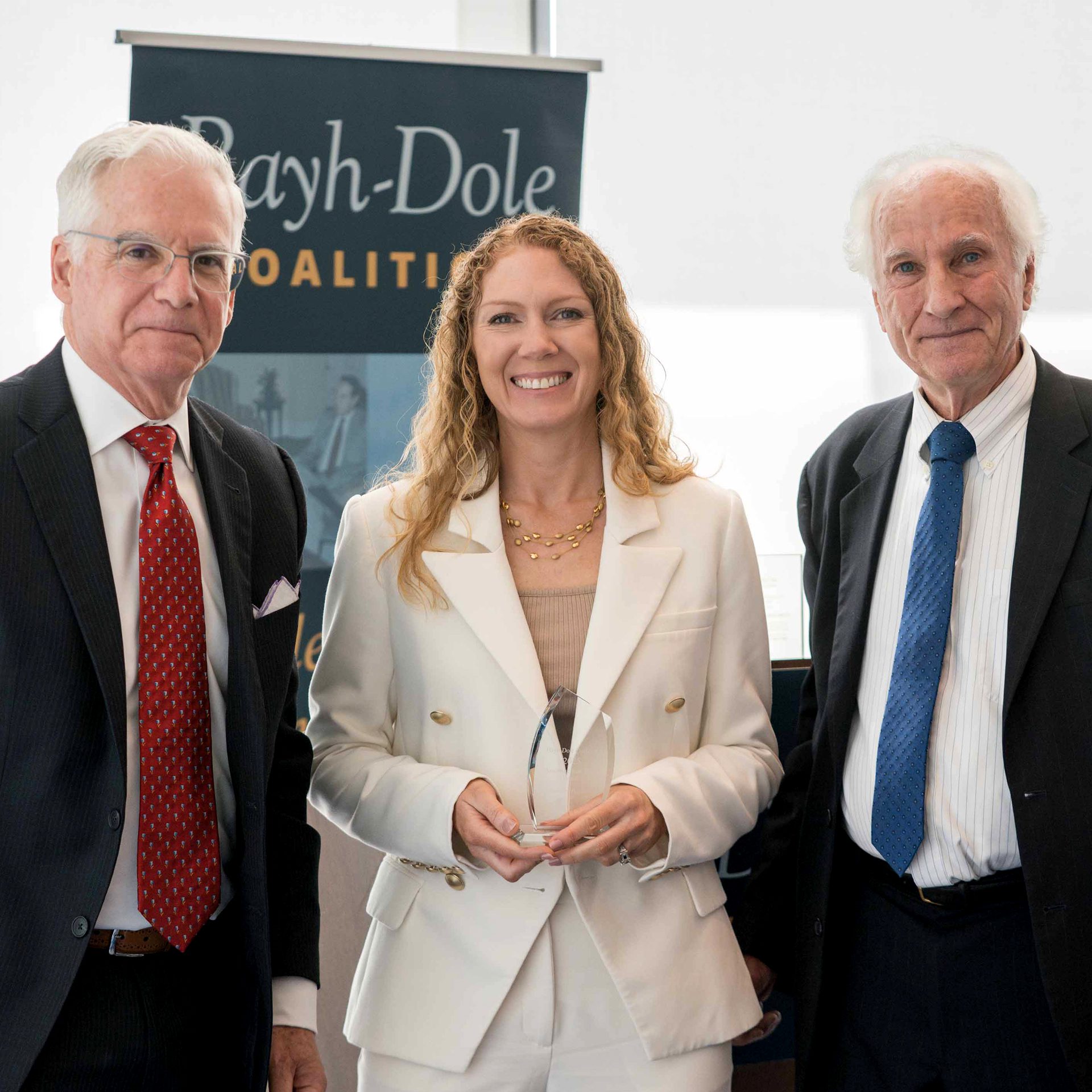 Three professionally dressed individuals stand together indoors in front of a 