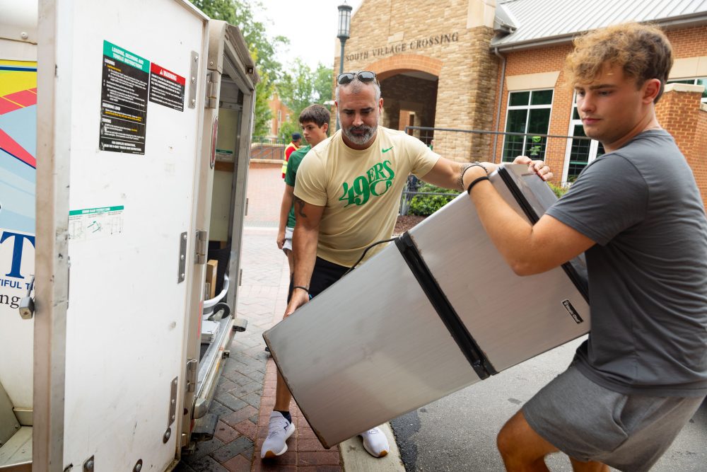 Niner and parent carry mini fridge in South Village 