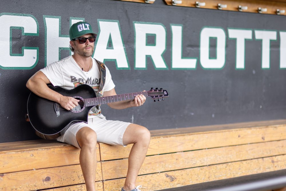 Chris Lane strumming a guitar in Charlotte baseball dugout