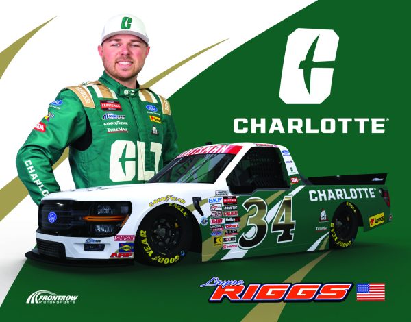 Layne Riggs '24 wearing a UNC Charlotte branded racing suit, standing behind a UNC Charlotte-wrapped truck