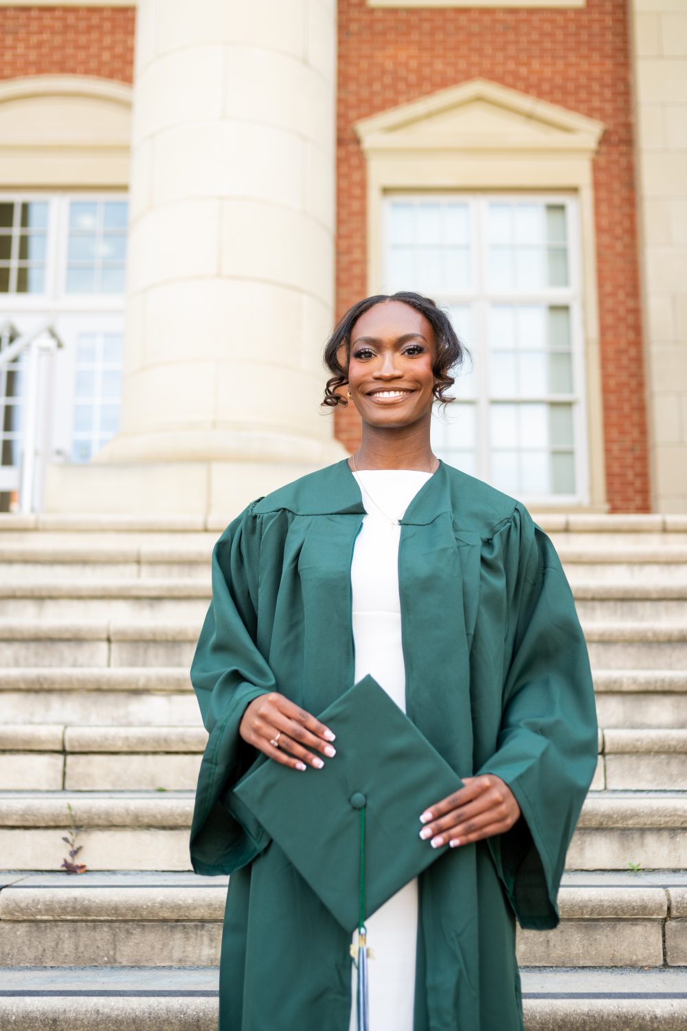 Kennedy Carpenter wears graduate gown and holds cap outside University building.