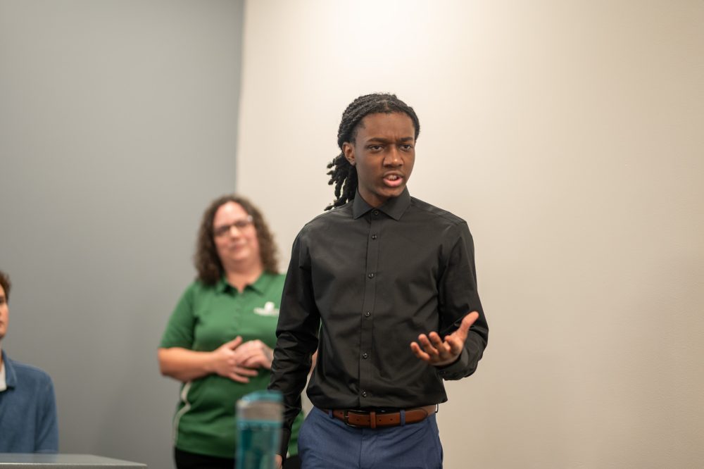 Jaylen Carroll holds his hand out illustrating his project at the Student AI Fellows showcase