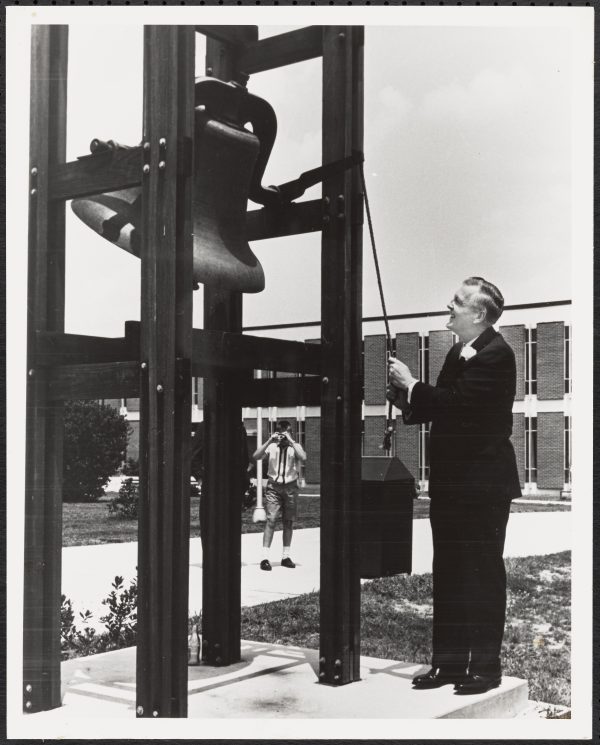 North Carolina Governor Dan Moore rings the Victory Bell at the dedication of Charlotte College as the University of North Carolina at Charlotte, July 1, 1965.