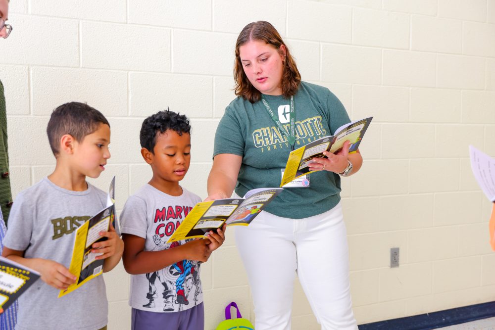Avery Larkin holds a book open and coaches two young students through a reading exercise