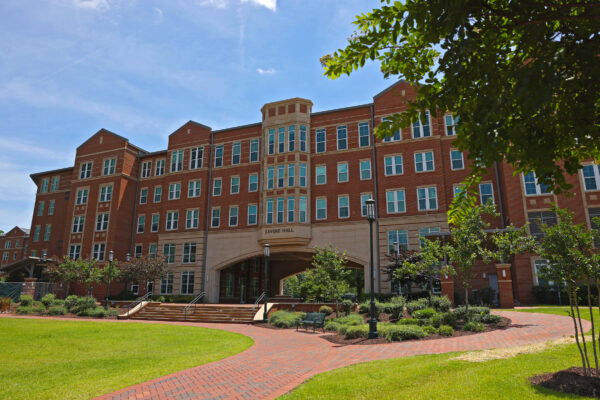 A red brick building labeled "Levine Hall" stands under a clear blue sky, surrounded by green lawns, paved walkways, and trees.