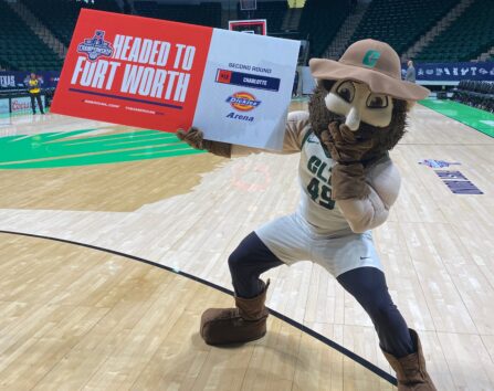 Norm the Niner holds a sign reading “Headed to Fort Worth” on a basketball court.