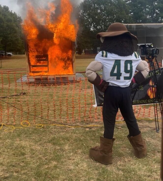 Norm the Niner watches a burning structure at a safety demo in the background.