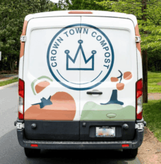 CT Van The back of a white Crown Town Compost van featuring a large blue crown logo and abstract shapes of fruits and vegetables, parked on a tree-lined street.