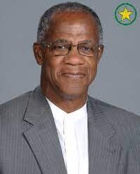 HermanThomas_UTOP_headshot A person in a gray suit and white shirt with a green circle and yellow star in the corner.