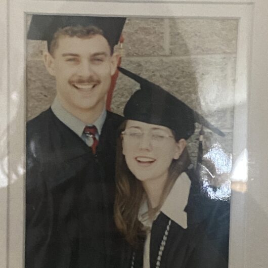Sharon-Williams-Niner-Love-Story-1 A framed photo shows two graduates wearing caps and gowns, standing close together and smiling.