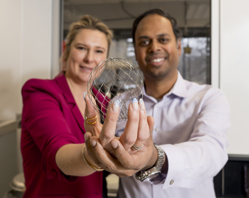 Two people in formal attire proudly holding a scientific object together in a laboratory setting.