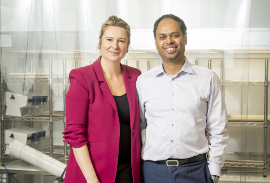 Two people standing in a laboratory with plastic strip curtains in the background.