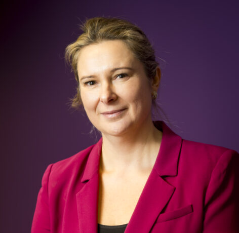 Portrait of a woman in a red blazer against a dark purple background.