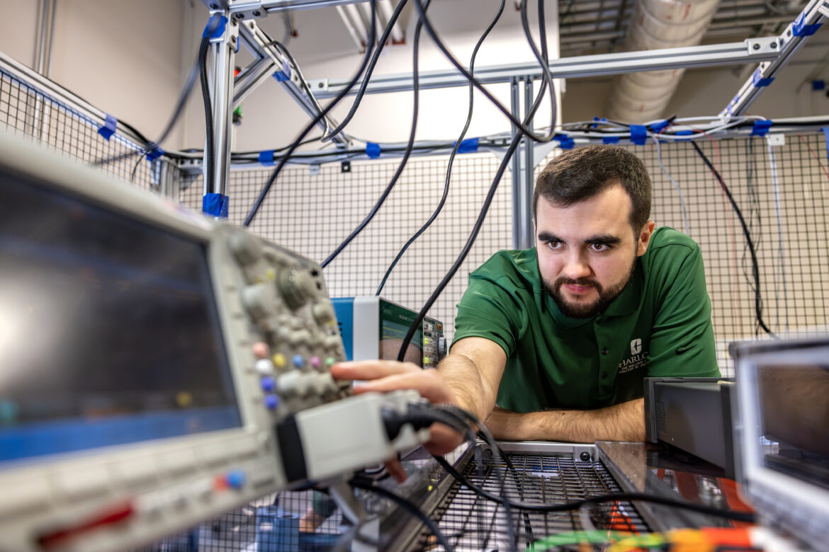 NSF-EPIC-Lab_260724_330 UNC Charlotte student wearing a College of Engineering polo leans over and adjusts equipment in EPIC Lab