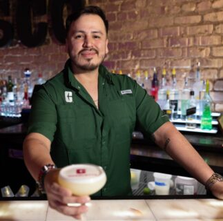 Man in green Charlotte polo shirt looking at the camera and holding out a cocktail.