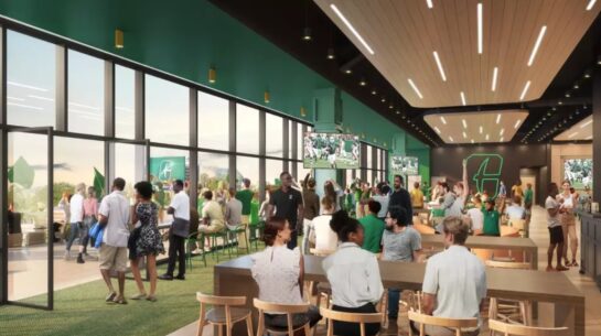 Rendering of the Terrace Club inside Jerry Richardson Stadium, showing a modern indoor hospitality space with floor-to-ceiling windows, dining tables, bar seating, televisions, and guests gathering before a football game.