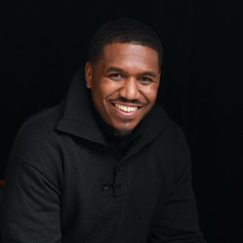 Ryan Walker, Matrix Marketing Portrait of a smiling man wearing a black sweater, seated in front of a solid black background.
