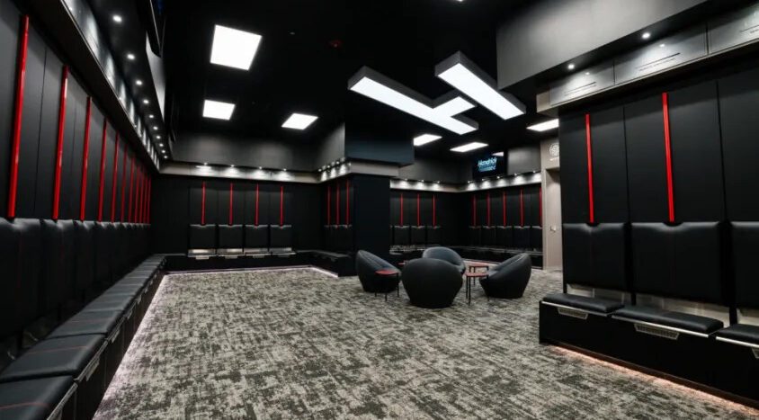 Modern Hendrick Motorsports locker room with black lockers, cushioned bench seating, lounge chairs, and contemporary lighting.