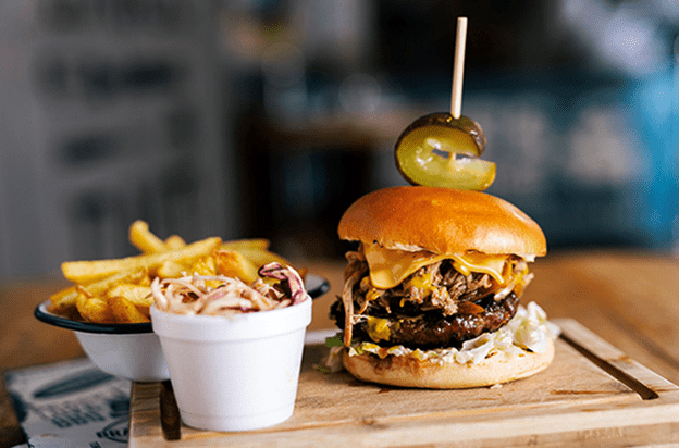 Cheeseburger with coleslaw and fries on a wooden board.