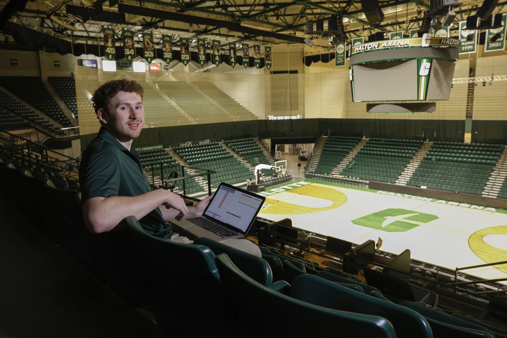 A guy with a laptop in an empty basketball arena.
