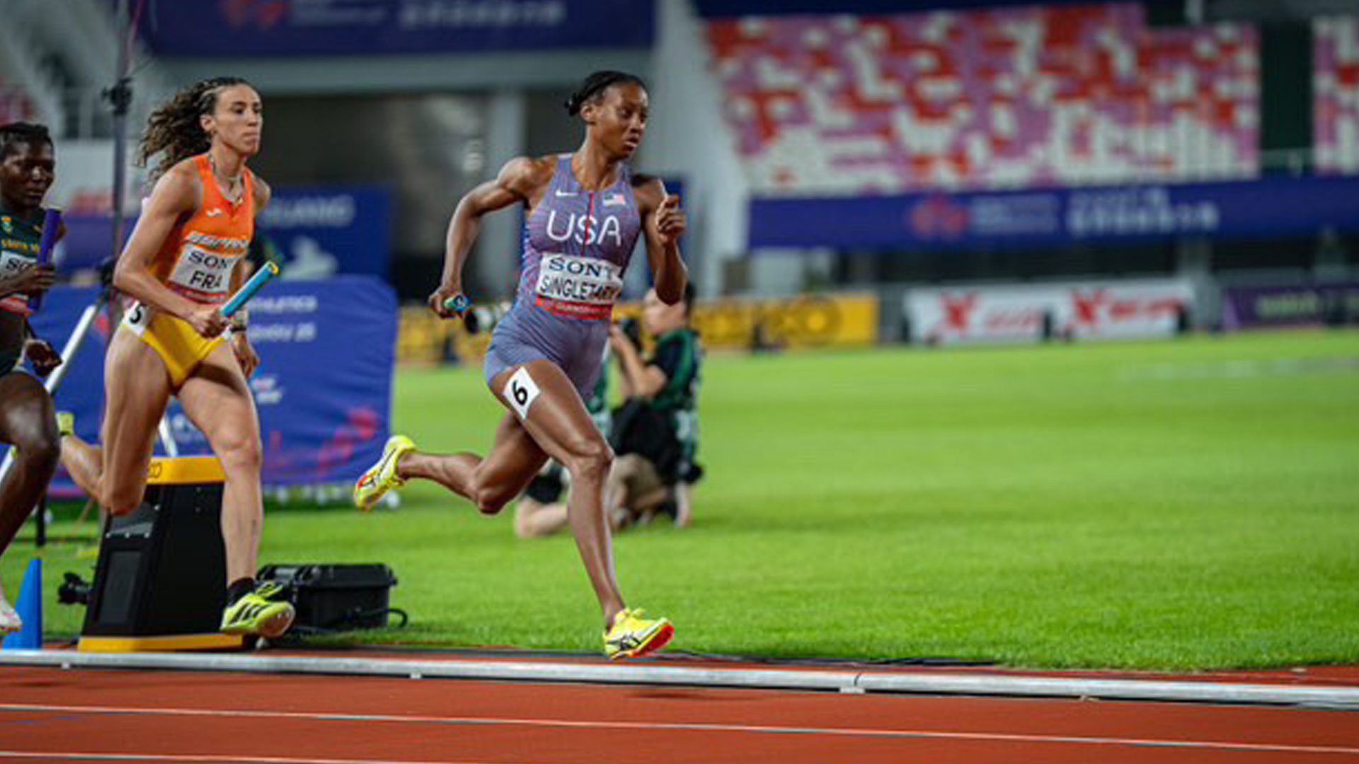 Team USA athlete runs in a relay race holding a baton.