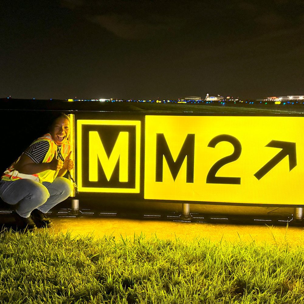 Myla Marve psoing by a runway sign at night