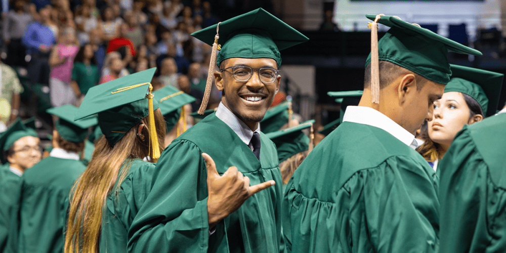 UNC Charlotte graduate hold hand up in the shape of a pickax wearing commencement regalia