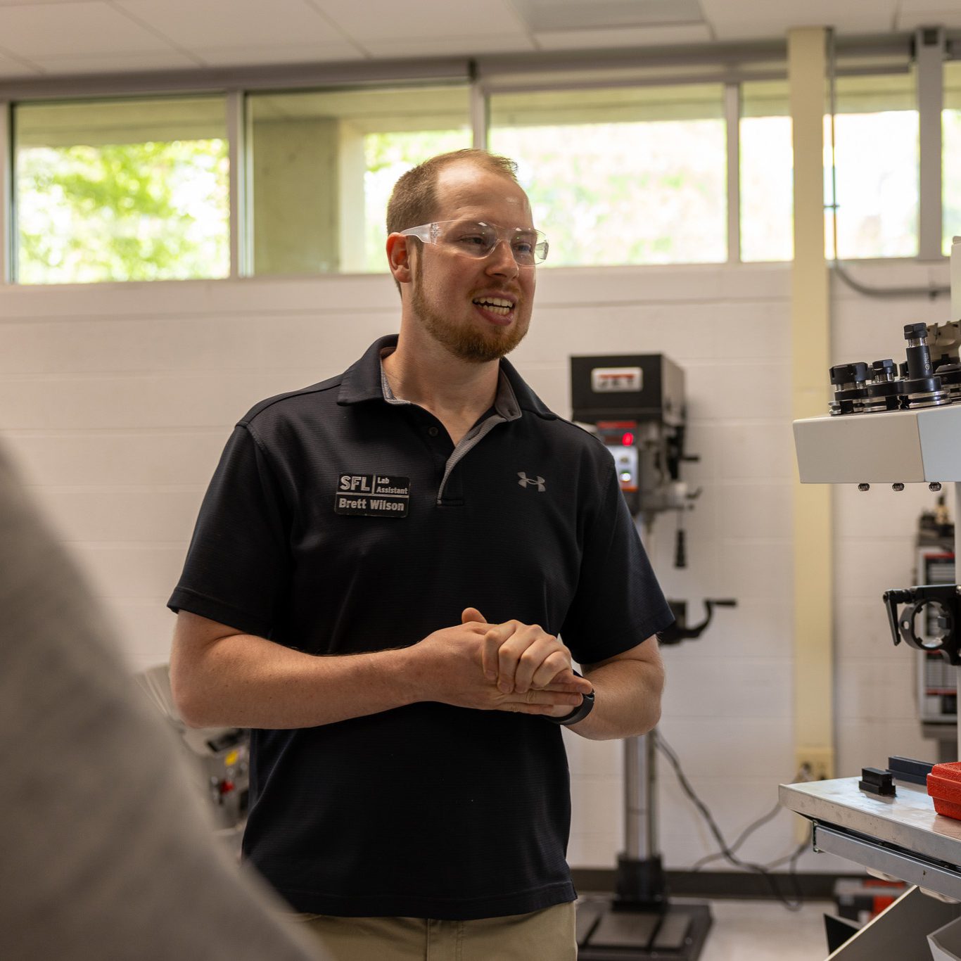Lab staff member wearing safety glasses speaks to a group inside a machining lab.