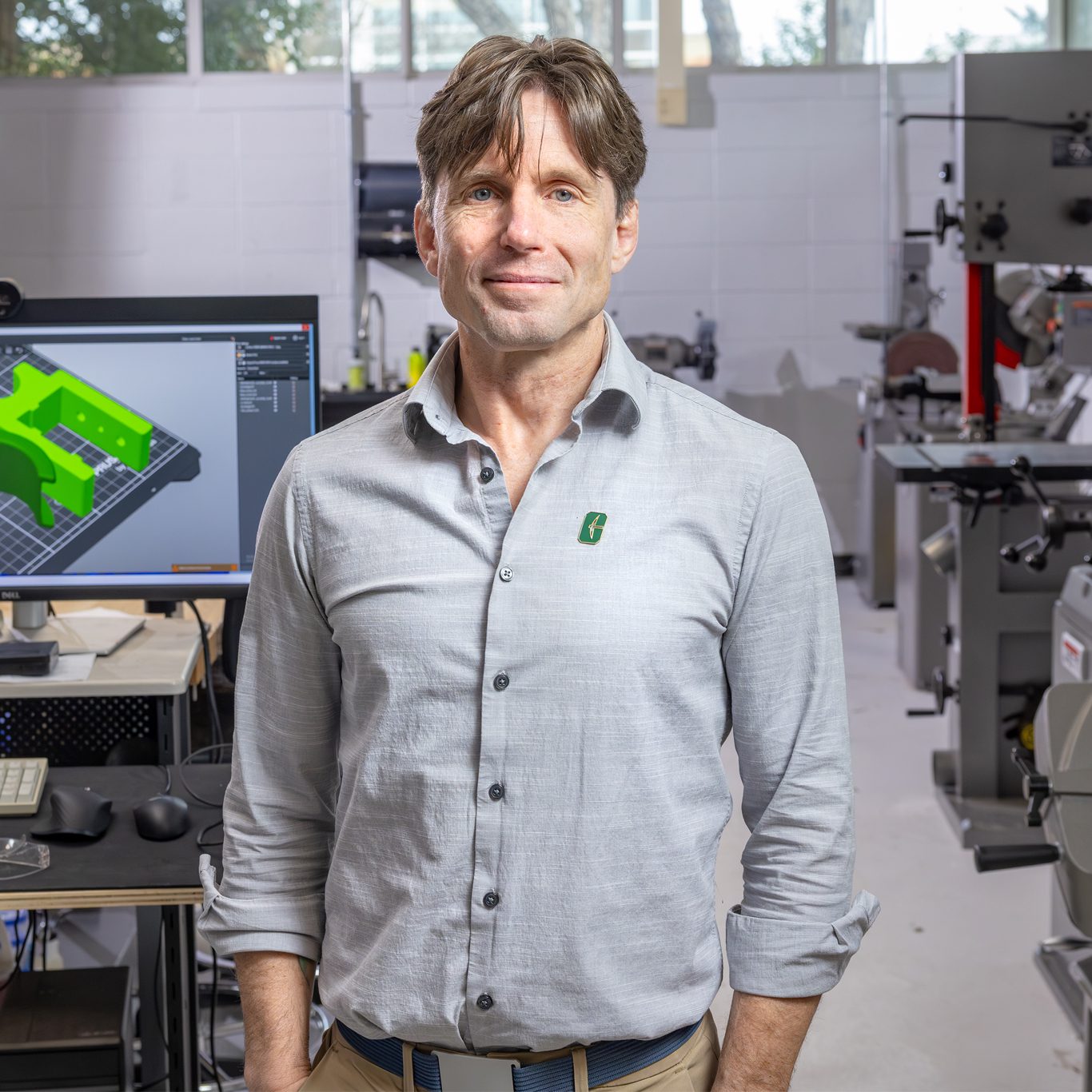 Man standing in a fabrication lab with a computer displaying a 3D model behind him.