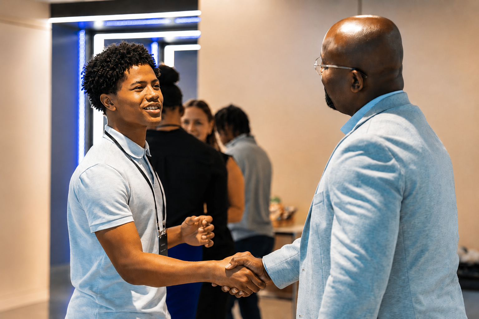 2026 Truist Report - Immersive 4 A student and a professional shake hands while smiling during a networking event. Other attendees converse in the background, highlighting a career-focused gathering that encourages professional connections and mentorship.