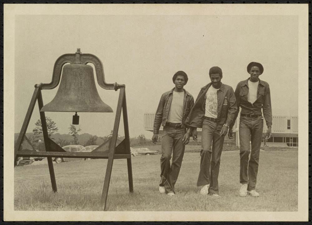Members of the Charlotte 49ers basketball team with the bell in front of Belk Gym.
