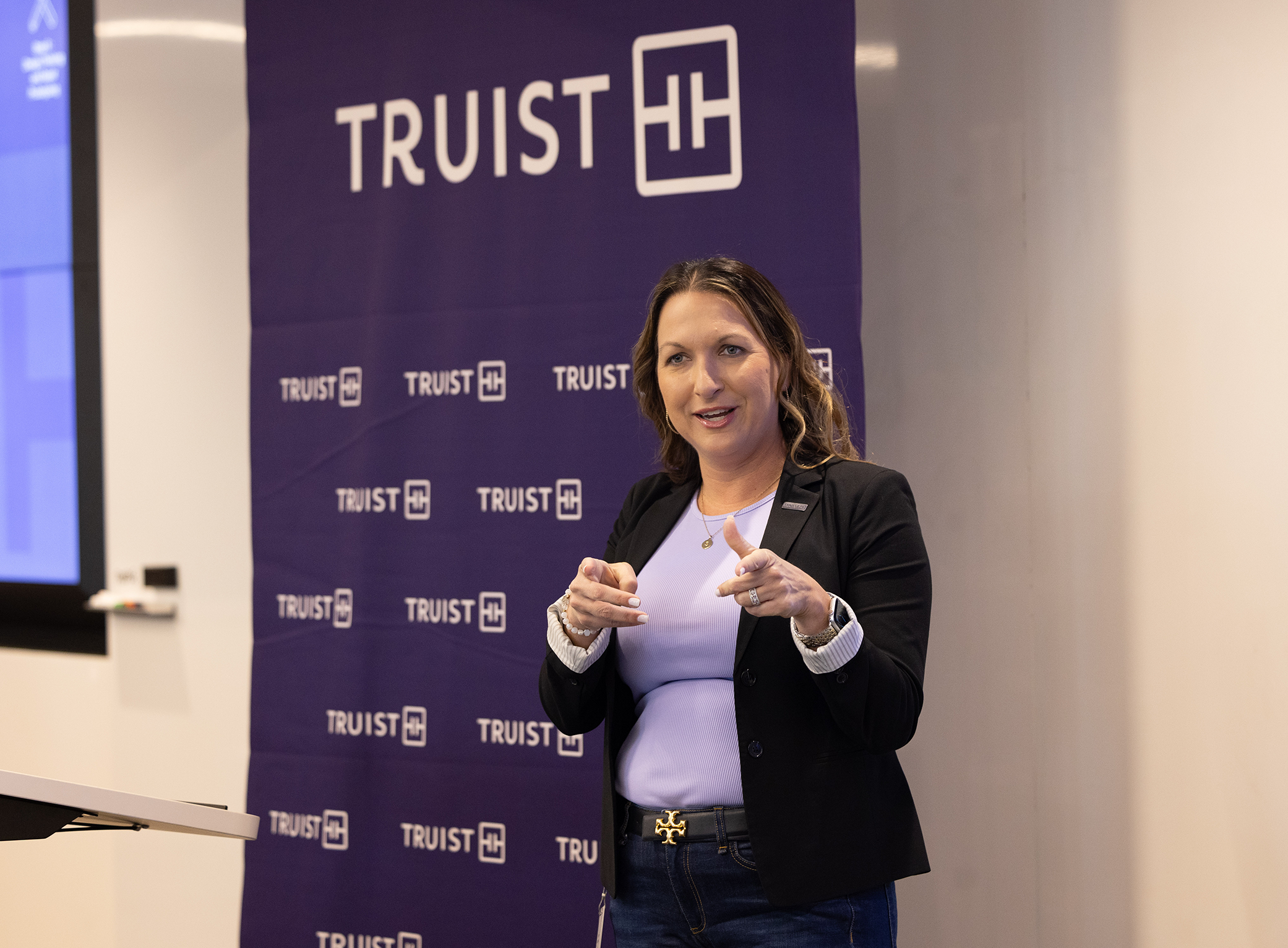 2026 Truist Report - Immersive 1 Speaker presents to an audience in front of a Truist-branded backdrop, gesturing while delivering remarks during a professional development or networking event.