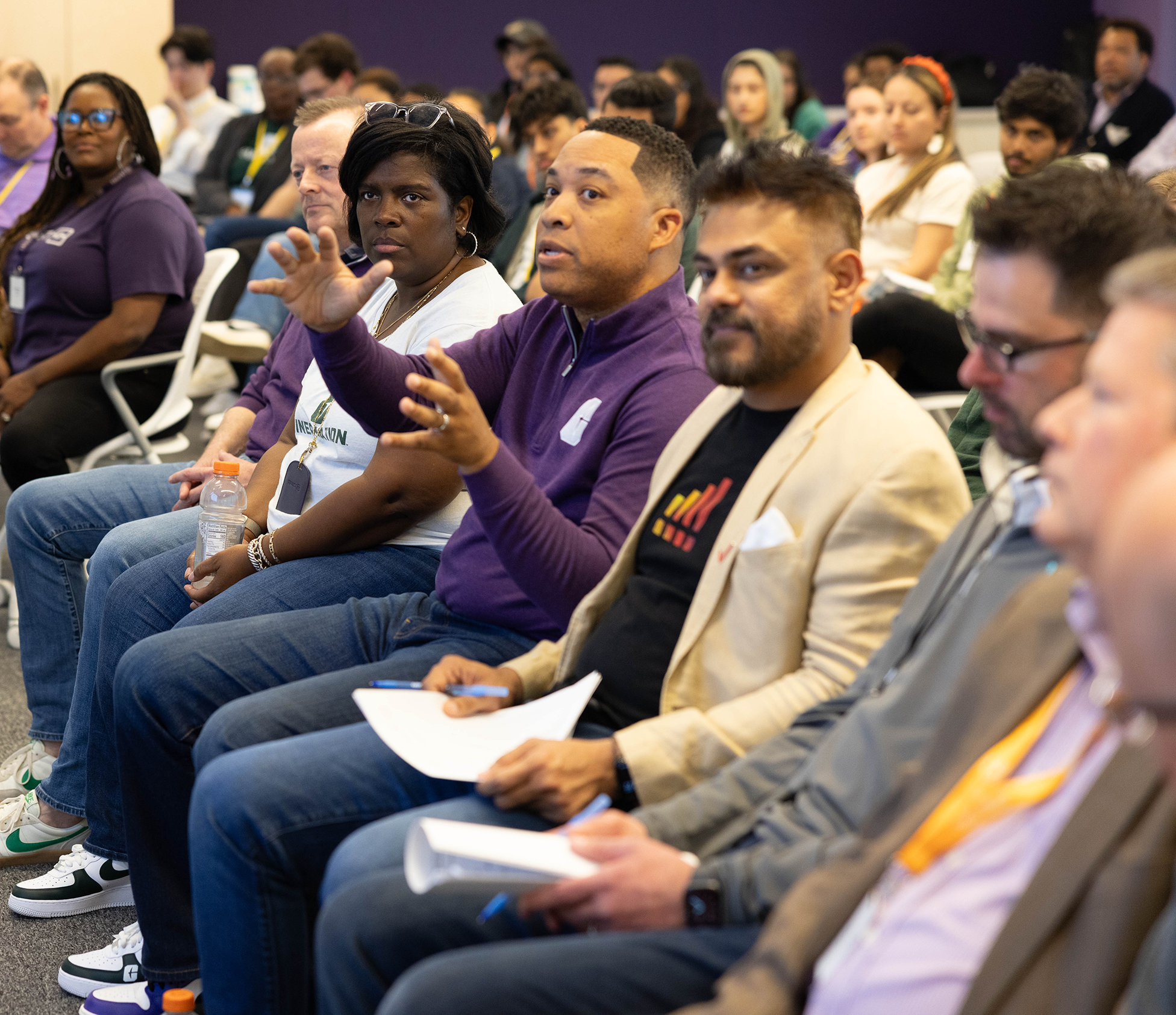 2026 Truist Report - Immersive 3 Audience members seated in a conference session as a man in a purple quarter-zip speaks and gestures with both hands during a group discussion, while attendees around him listen and take notes.