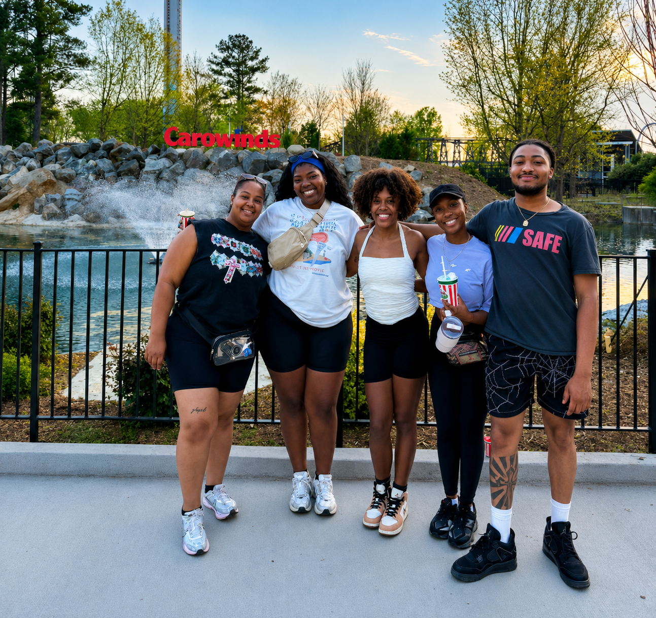 2026 Truist Report - SAFE Five friends stand arm in arm, smiling for a photo in front of a fountain and the Carowinds sign, with trees and amusement park attractions visible in the background at sunset.