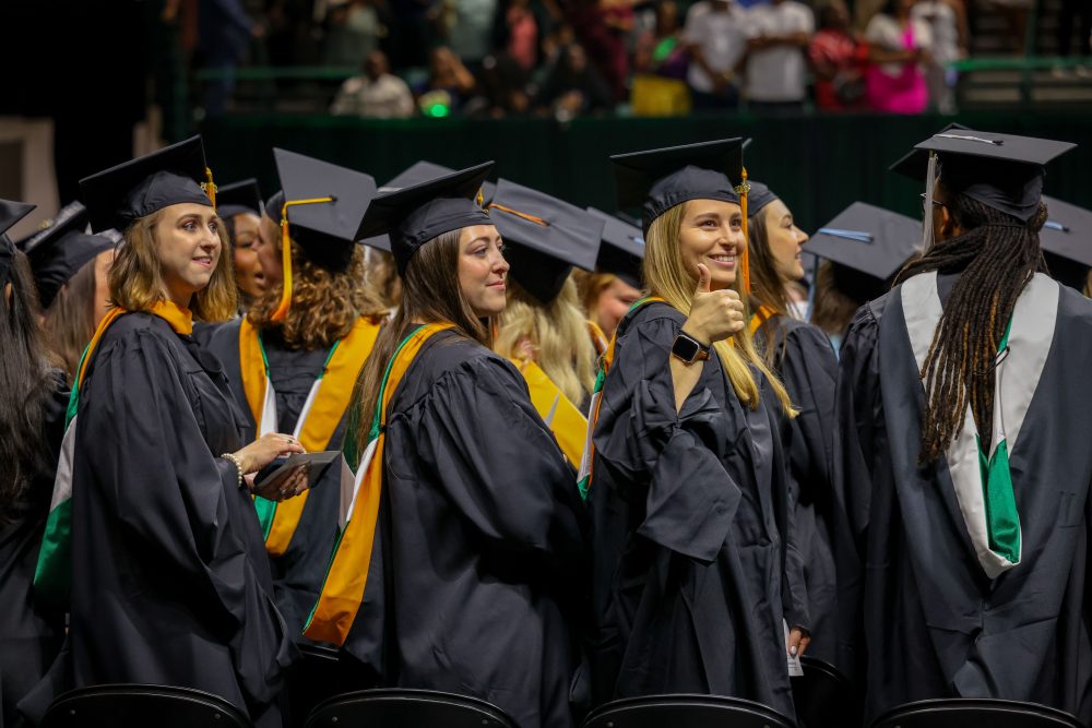 A master's degree graduate gives a thumbs up sign.
