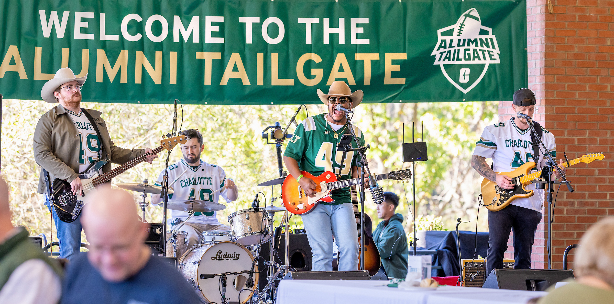 Homecoming_24117_r520_rh (1) A band performs on stage at an alumni tailgate event under a green banner.