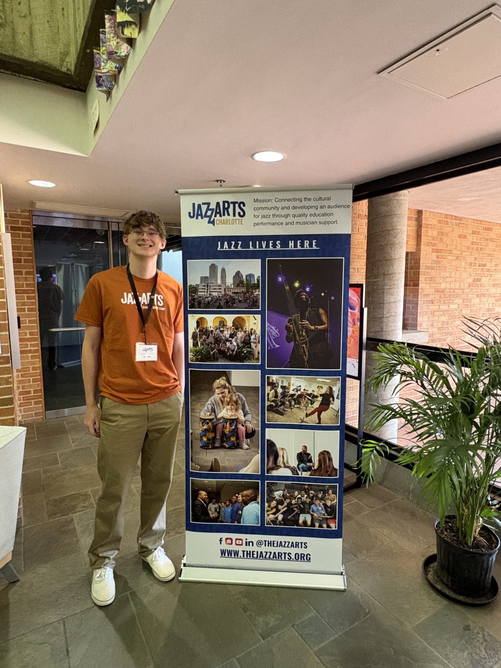 Rex Jacobs stands next to JazzArts Charlotte poster